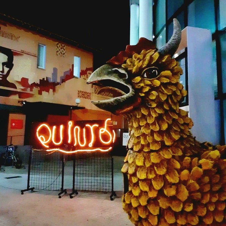 Entrada del Centre Cultural amb el rètol de neó del Quinto i el Poll Foc en primer pla, al costat de la porta