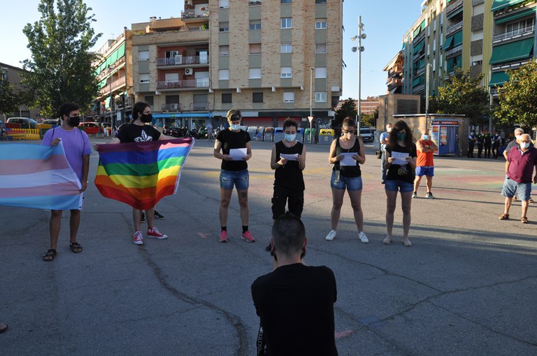 Proud LGTBI Ripollet llegint el manifest contra la LGTBI-fòbia amb les banderes de l'arc de Sant Martí i la bandera del col·lectiu Trans